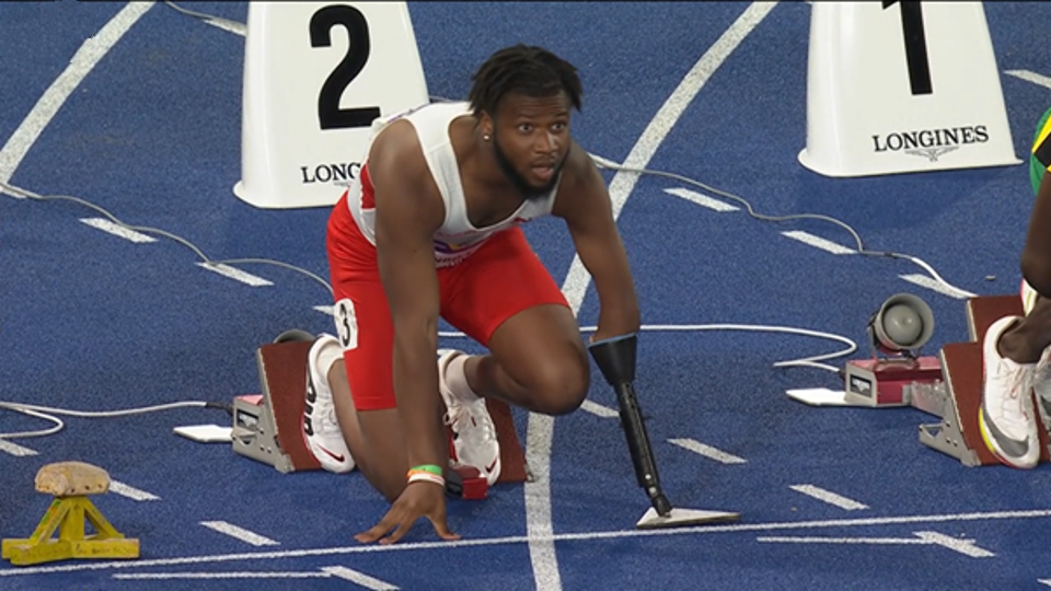 An image showing Emmanuel Oyinbo-Coker at the start line of the T45-47 100m at the Birmingham 2022 Commonwealth Games, he is wearing a prosthetic starting device designed by graduate Neve Deal.